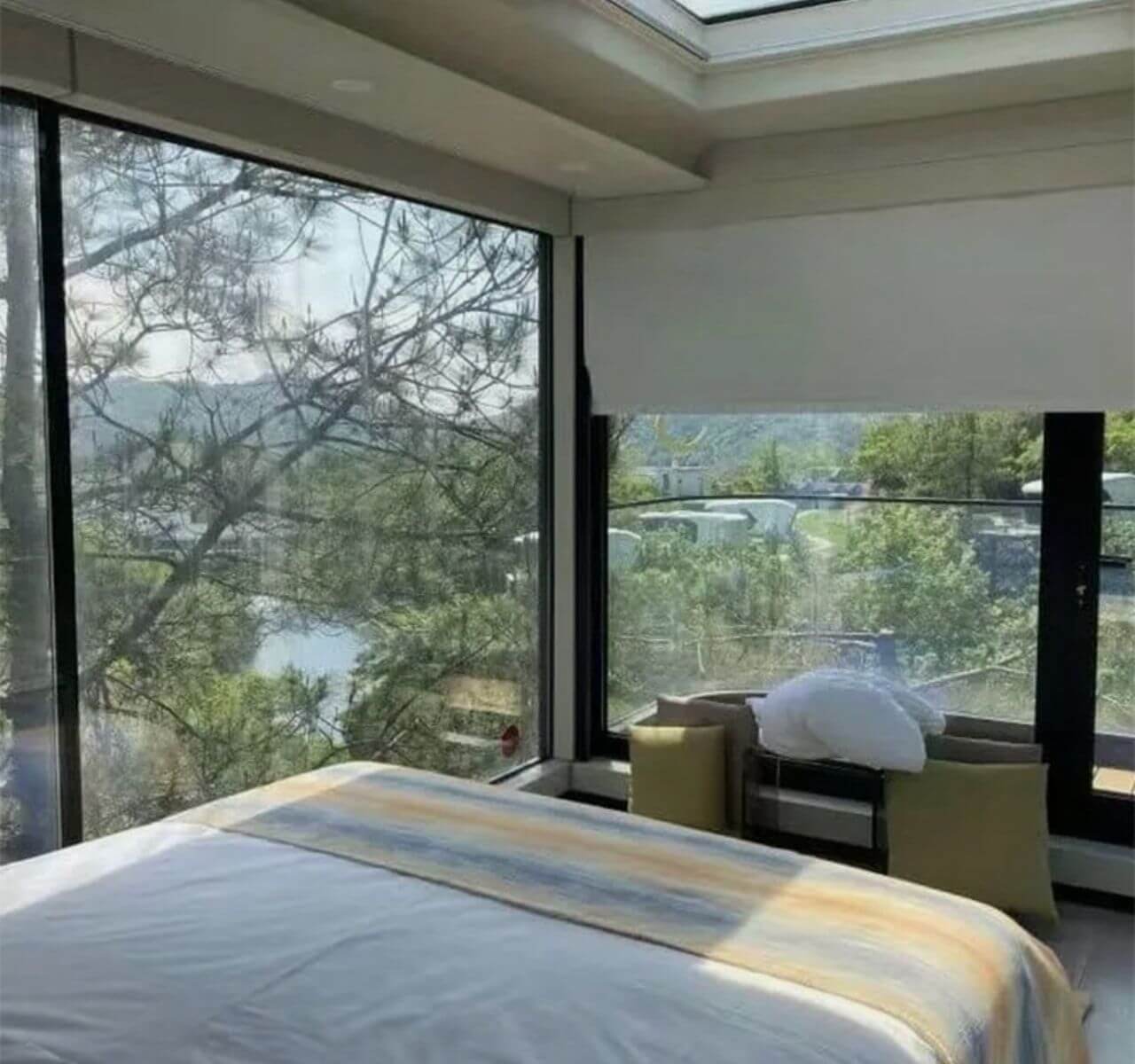 Spacious luxury bedroom with large windows overlooking greenery and water, featuring a sleek modern design.